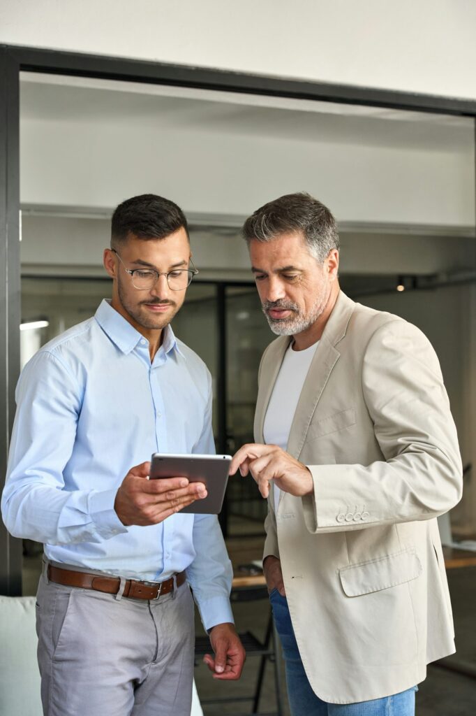 Busy executive business team of two men working on tab standing in office.